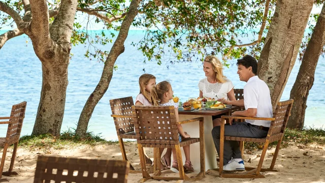 Famille profitant d'un déjeuner extérieur les pieds dans le sable au Sand Beach Grill Sheraton New Caledonia Deva Spa & Golf Resort