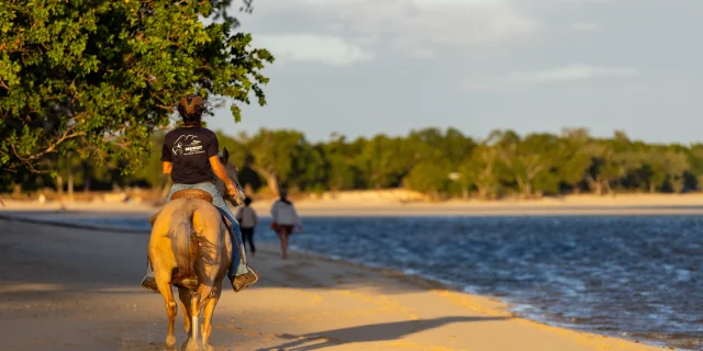 Femme à dos d'un cheval parcourant la plage de Bourail au coucher du soleil